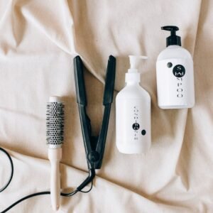 Flat lay of hairbrush, hair iron, and shampoo bottles on fabric background.